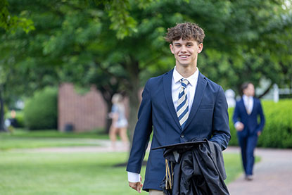 A proud student holds his graduation cap and gown in his hand. Links to Gifts That Pay You Income